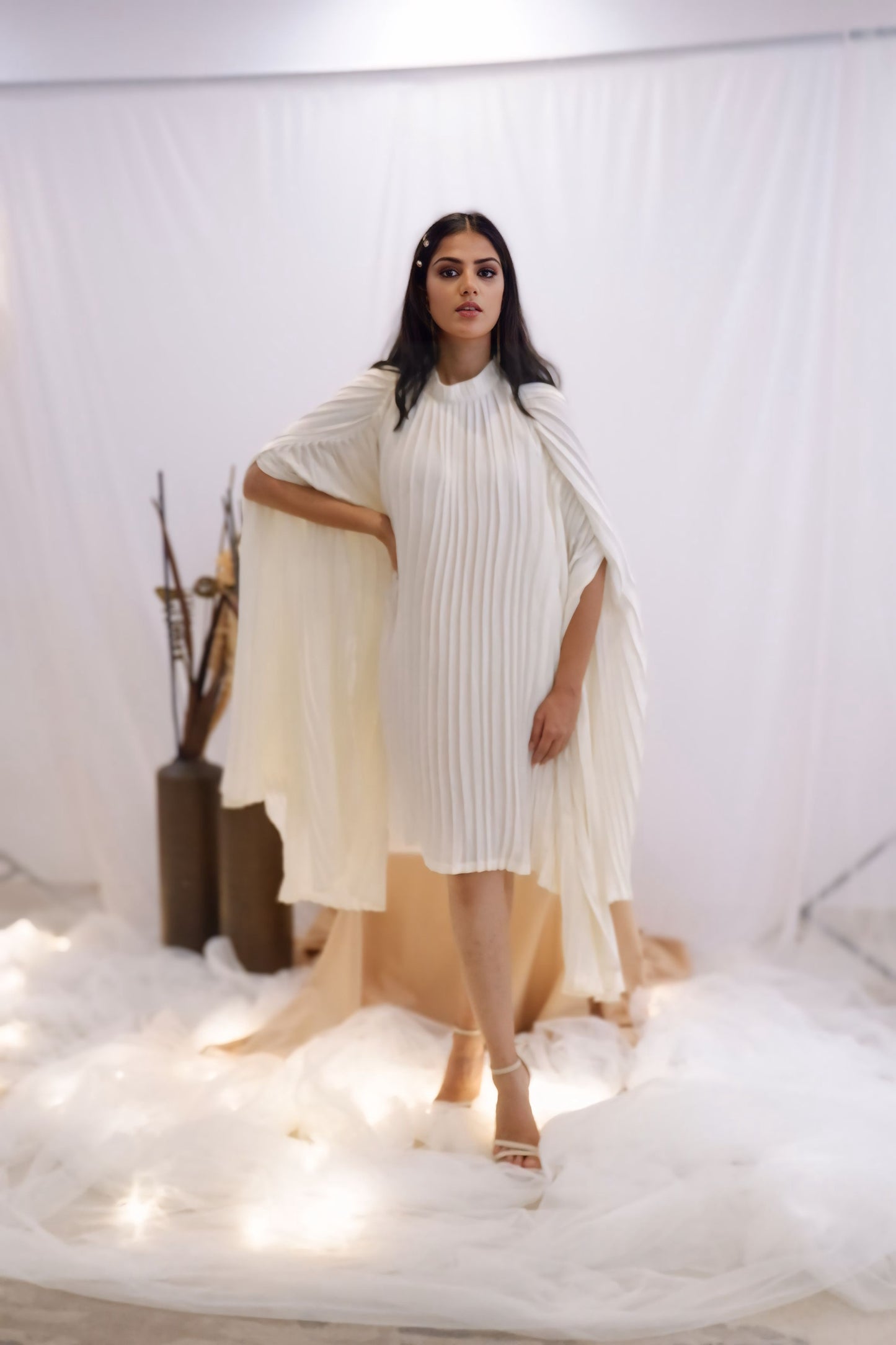 Woman wearing a white pleated dress in a minimalistic setting. Freo