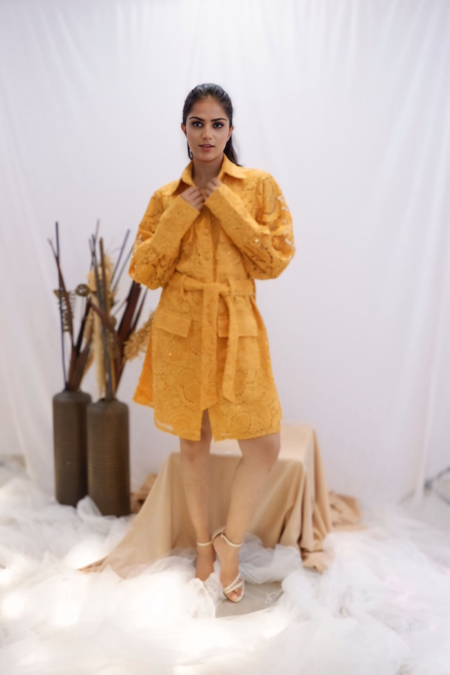 Woman wearing a yellow outfit standing in a minimalistic setting with white background and decorative elements. Freo