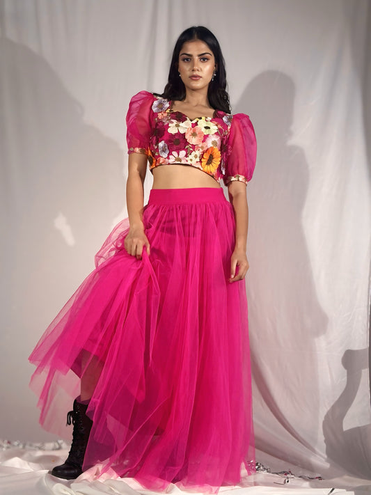 Woman wearing a colorful floral top and bright pink skirt against a plain background