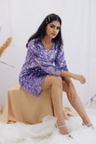 Woman in a purple sequin dress sitting on a white surface with a neutral background