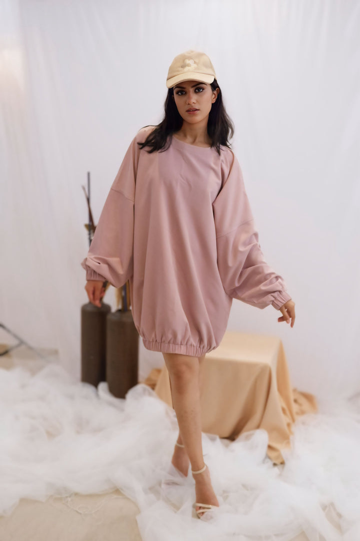 Woman wearing a pink dress and beige cap in a minimalistic setting with white background