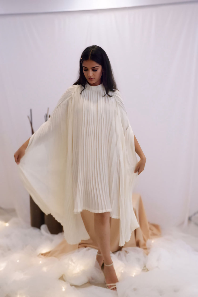 Woman wearing a white pleated dress in a minimalistic setting. Freo