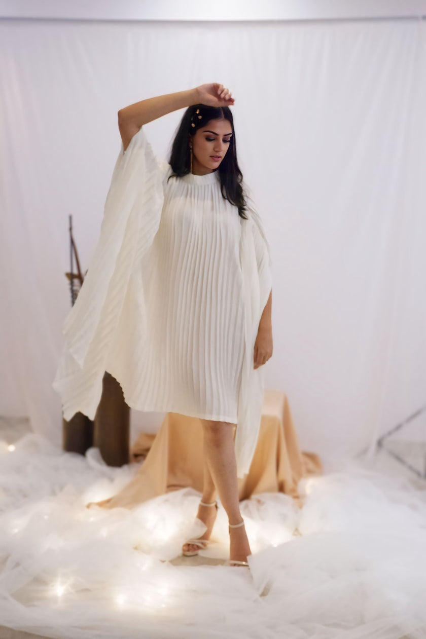 Woman wearing a white pleated dress in a minimalistic setting. Freo