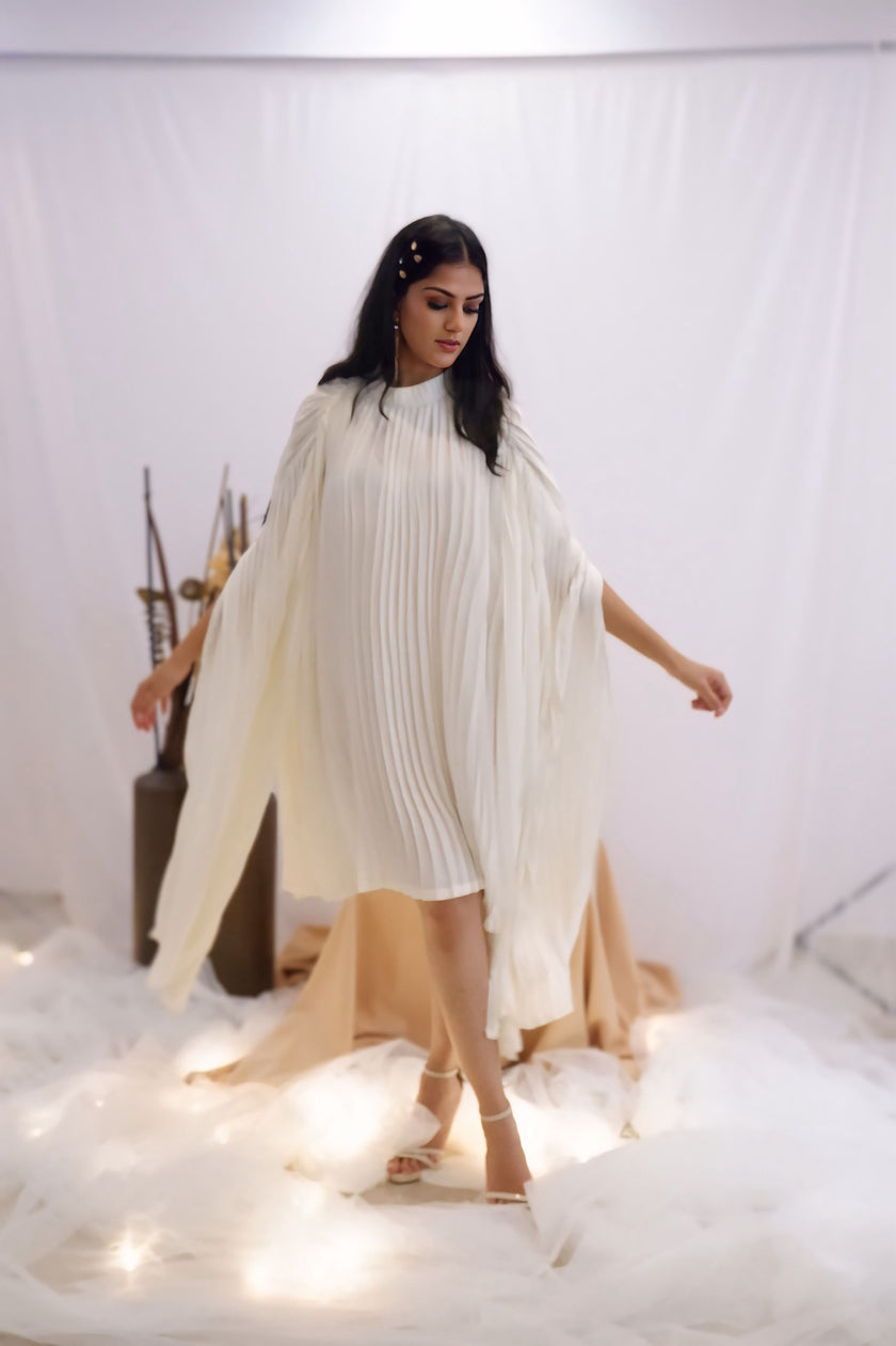 Woman wearing a white pleated dress in a minimalistic setting. Freo