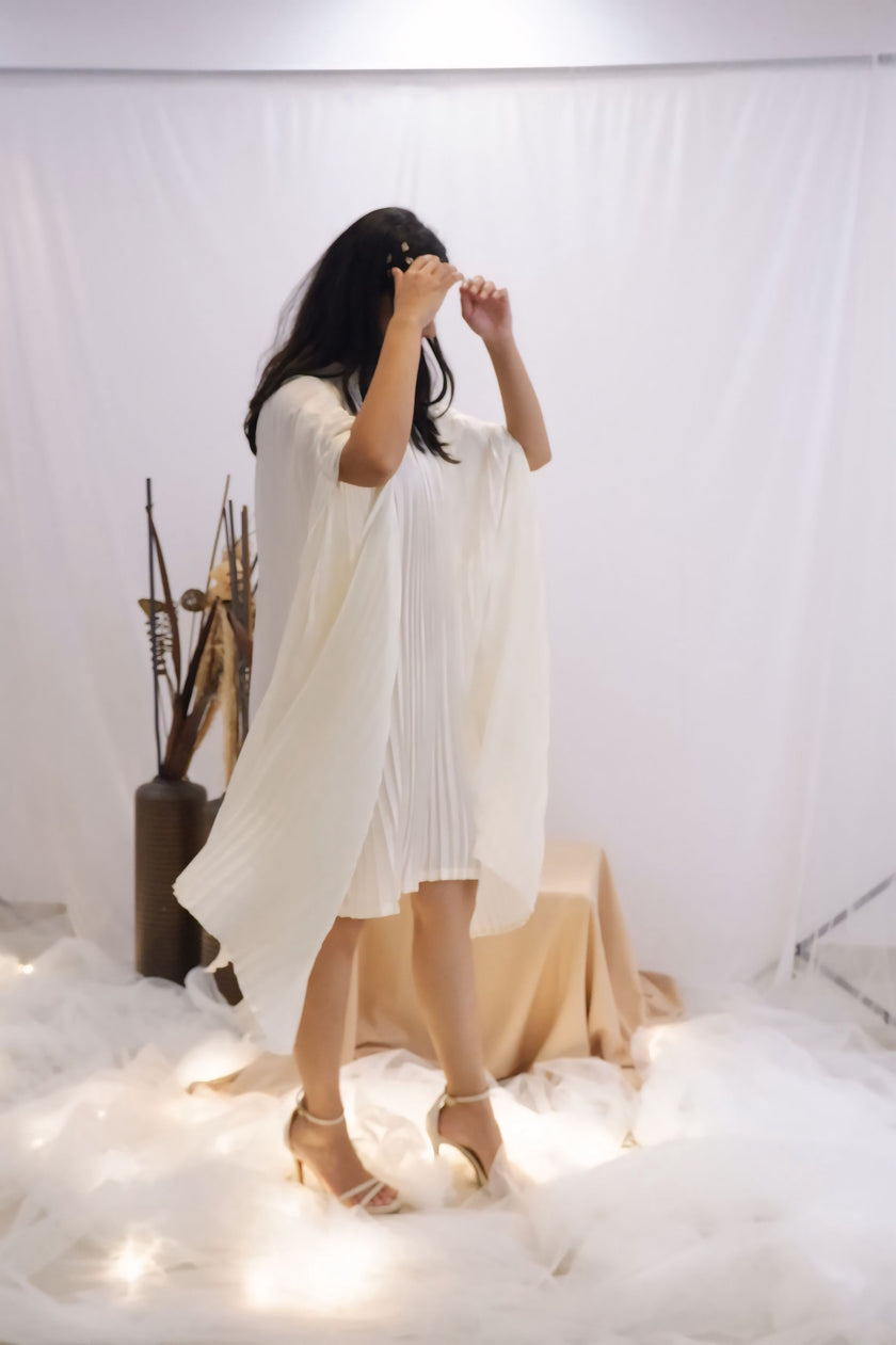 Woman wearing a white pleated dress in a minimalistic setting. Freo