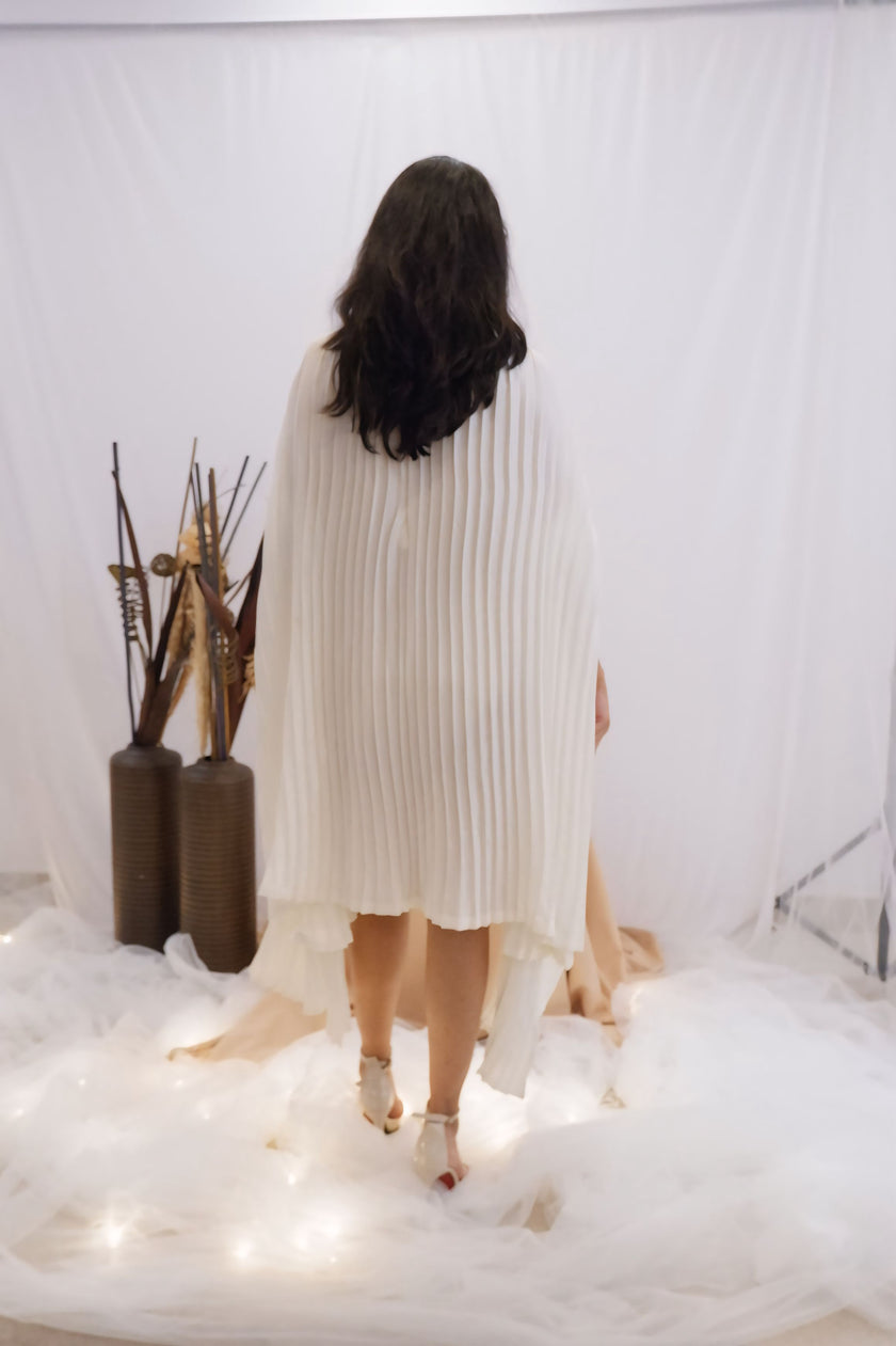 Woman wearing a white pleated dress in a minimalistic setting. Freo