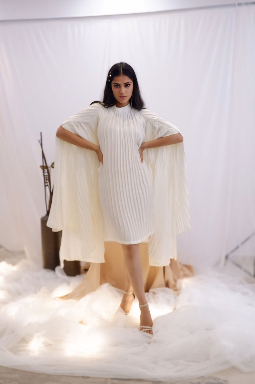 Woman wearing a white pleated dress in a minimalistic setting. Freo