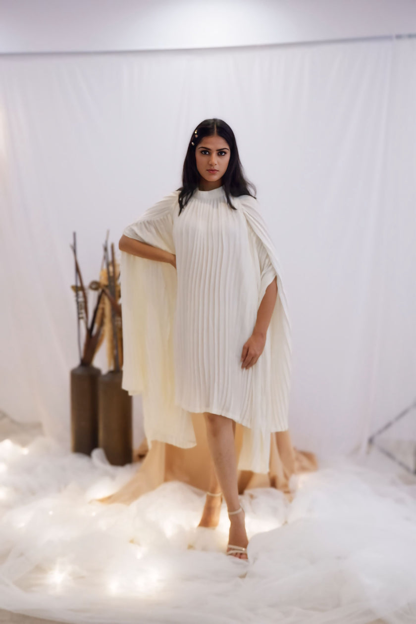 Woman wearing a white pleated dress in a minimalistic setting. Freo