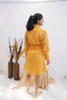 Woman wearing a yellow outfit standing in a minimalistic setting with white background and decorative elements. Freo
