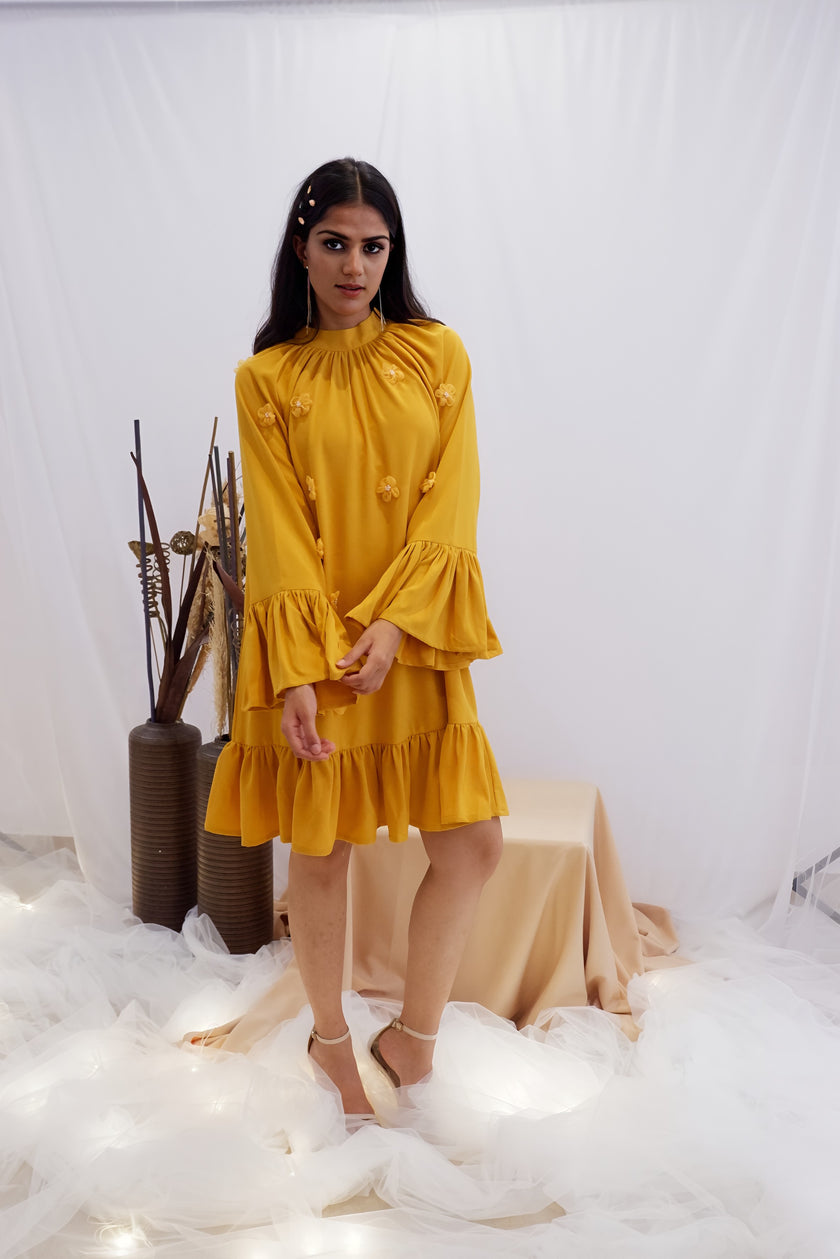 Woman wearing a yellow dress standing in a softly lit room with decorative elements. Freoi