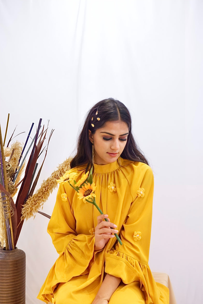 Woman wearing a yellow dress with floral details against a white background. Freo