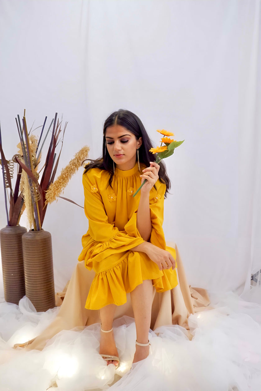 Woman wearing a yellow dress with floral details against a white background. Freo
